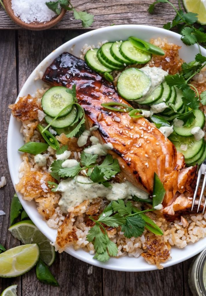 Salmon in a bowl of crunchy brown rice with cucumber slices.