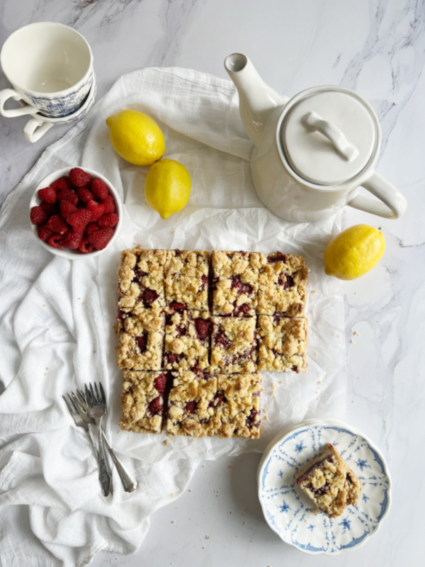 Lemon Raspberry Crumble Bars cut with a white teapot and some blue and white dishes.