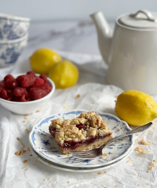 Friday Favorites Lemon raspberry bar on a blue and white plate with scattered lemons and a white teapot.