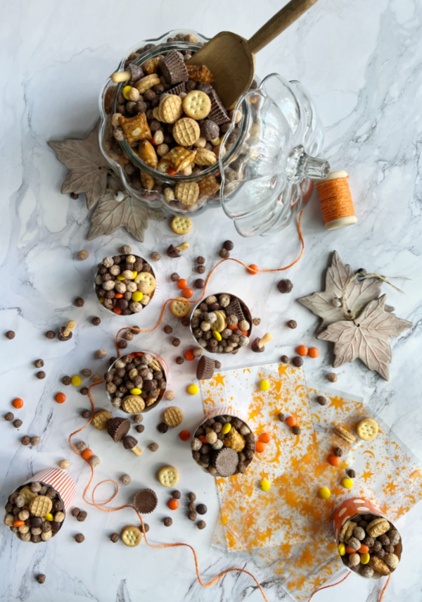 Peanut Butter Fall Snack mix in a pumpkin and scattered with orange twine and cellophane bags.