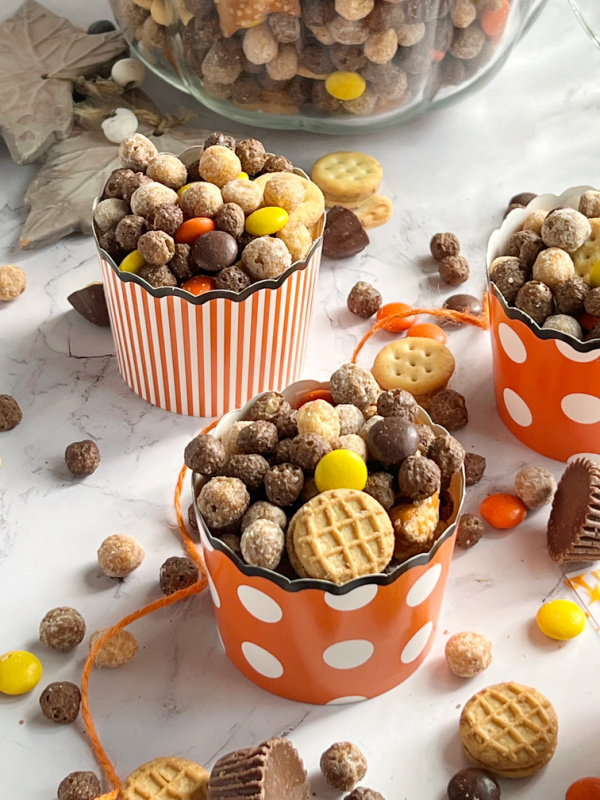 Peanut Butter Fall Snack mix in a pumpkin and scattered with orange twine and orange and white paper cups.