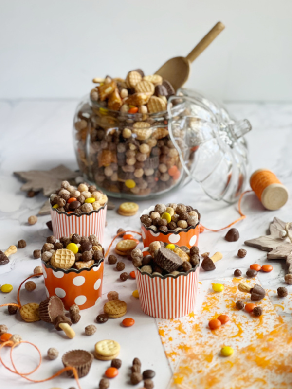 Peanut Butter Fall Snack mix in a glass pumpkin and small orange and white cups.