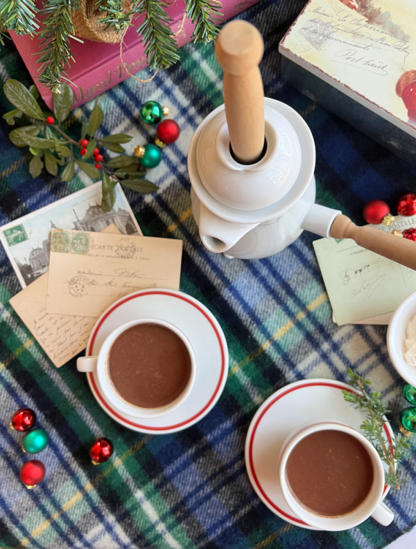 French hot chocolate in two cups with French post cards and a white chocolate pot.
