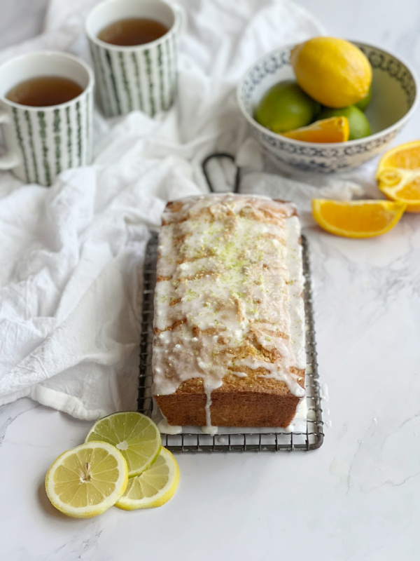 Triple Citrus Quick Bread with two cups of tea and a small bowl of limes, lemon and sliced oranges.