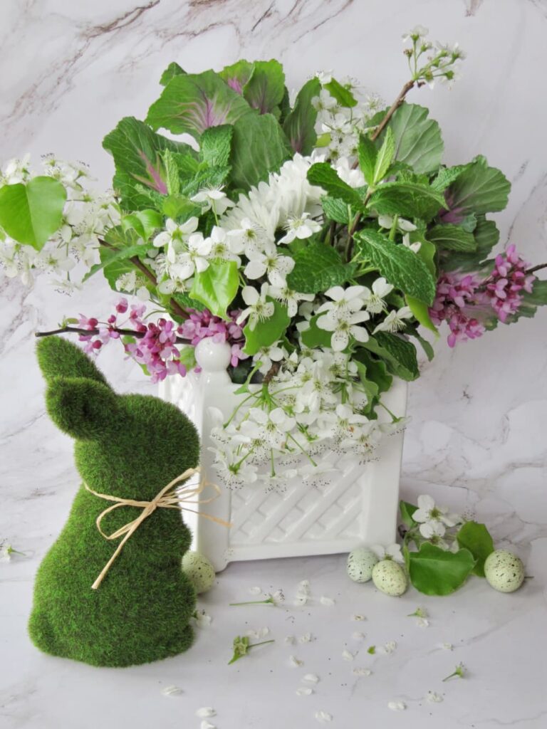 Green Easter bunny and a white planted filled with colorful pink and white and green flowers.
