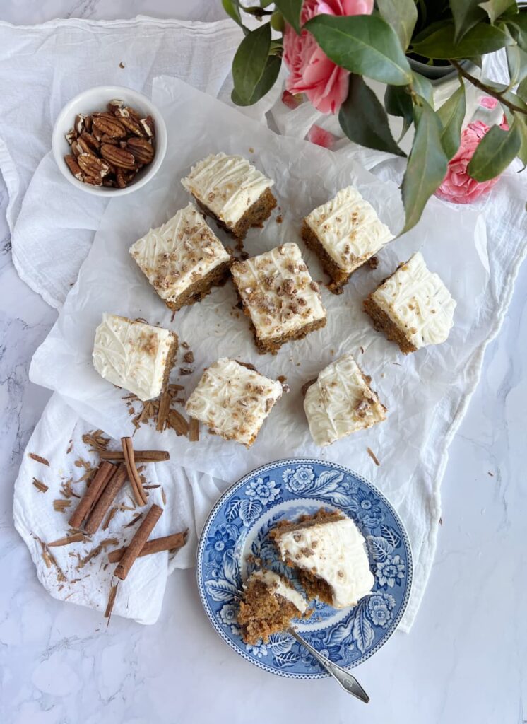 carrot cake with cream cheese frosting on a blue and white plate with toasted pecans.