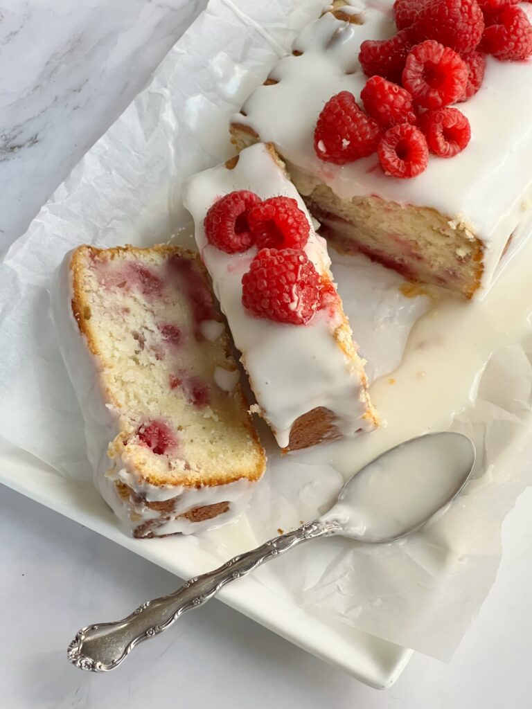 Raspberry Lemon Loaf Cake sliced on a white platter with a spoon full of lemon icing.