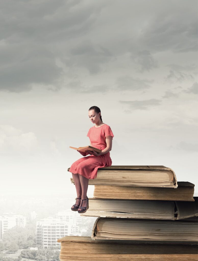 small woman sitting on a stack of books reading.
